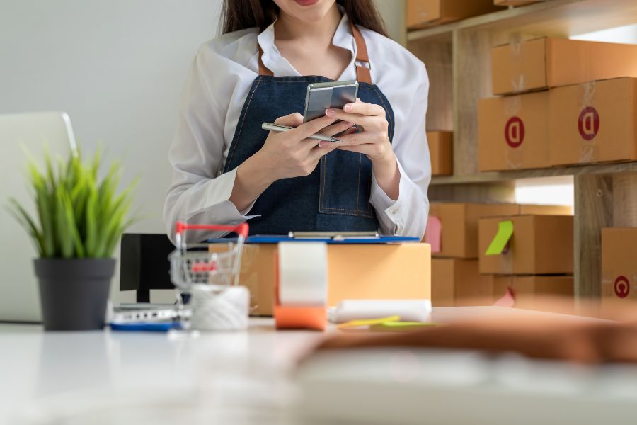 A woman managing an online store with a smartphone in a small business warehouse.