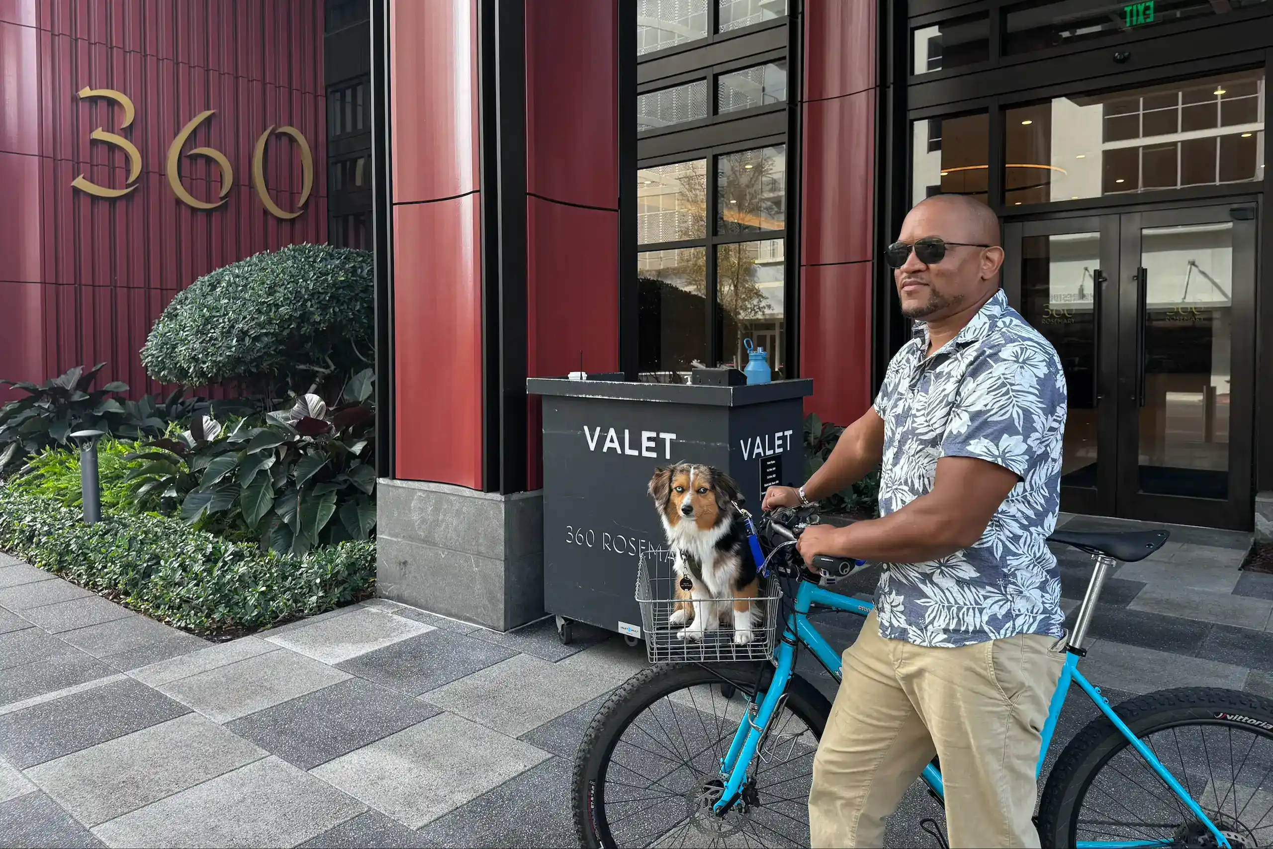 Man with dog on bike outside 360 Rose building in downtown.