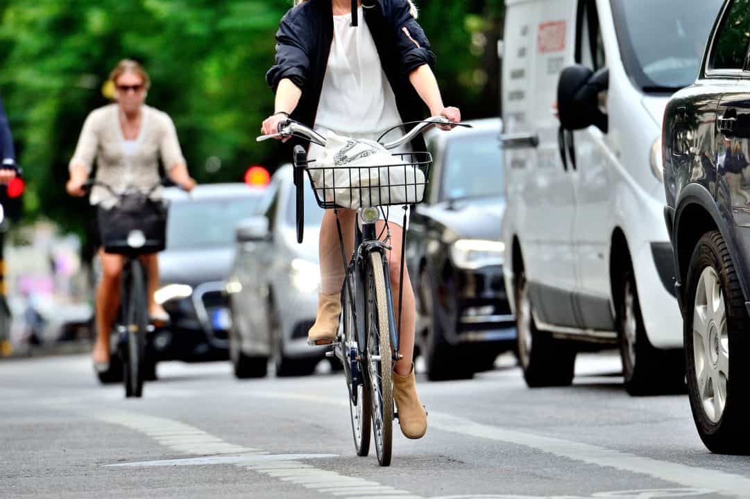 Cyclist riding bike on busy city street with cars and pedestrians.