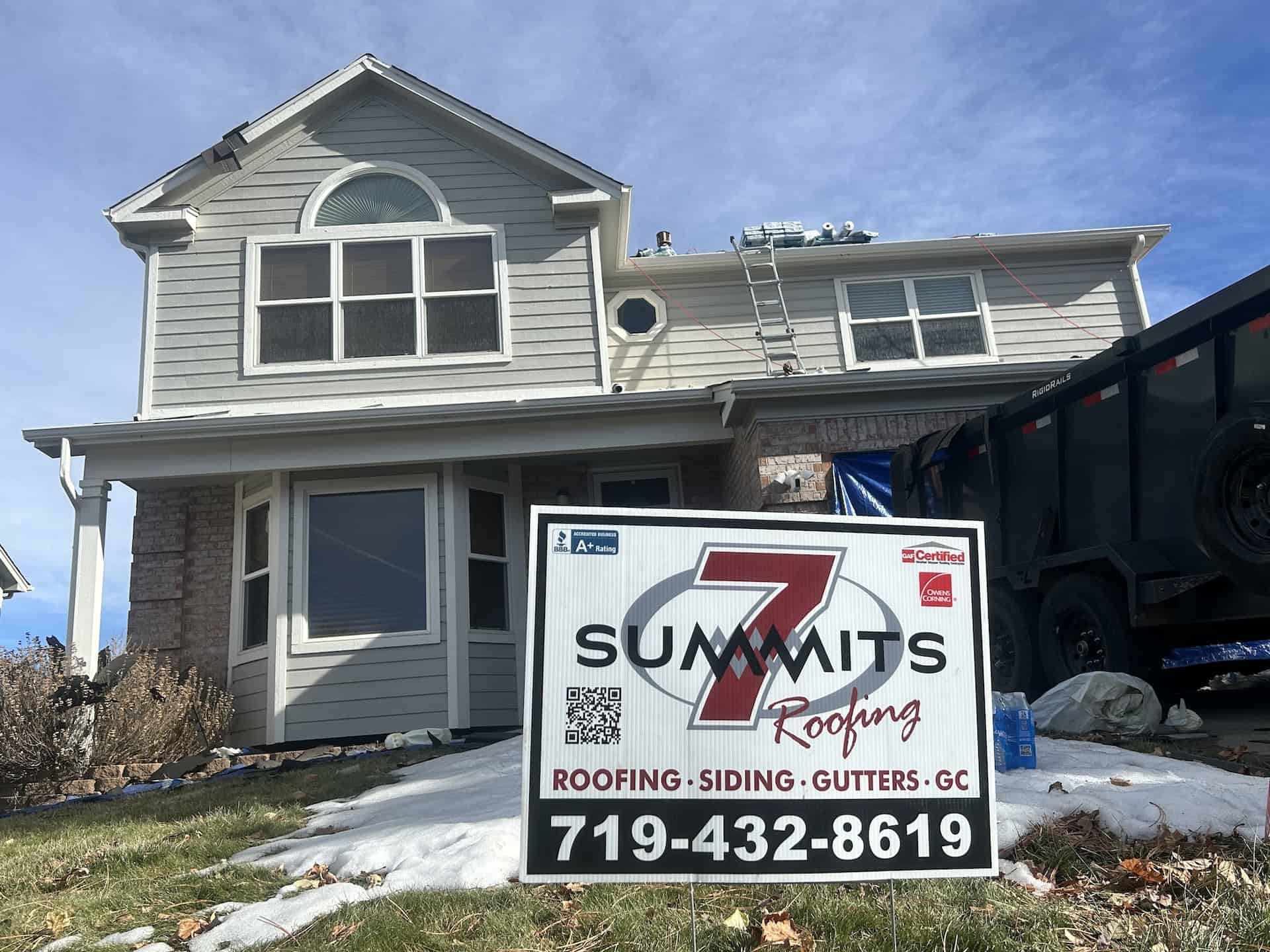 Suburban two-story home in process of roof removal with 7 Summits Roofing sign in the yard.