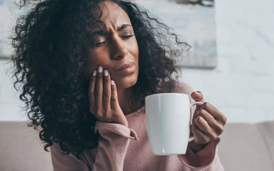 woman touching face after biting her cheek and holding a cup of coffee