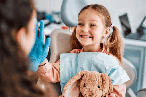 A child holding a toy rabbit smiles and gives her dentist a high five.