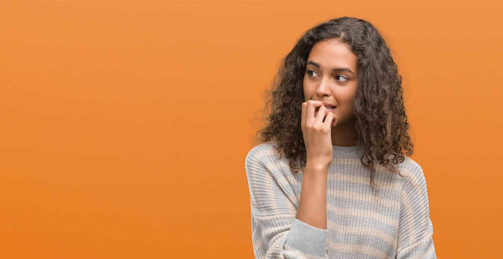 nervous woman with fingers on her lips, looking to the side, on orange background