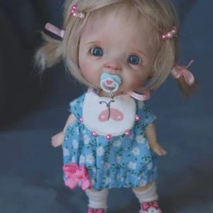 A doll ob11 with a pacifier and a blue dress.