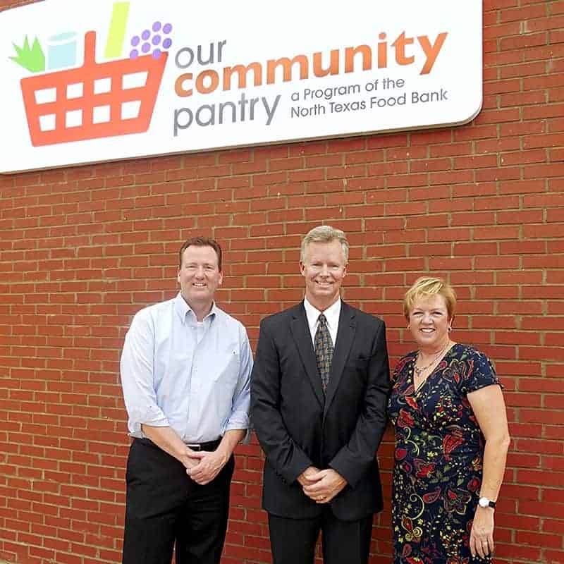 Three people in front of food bank sign.