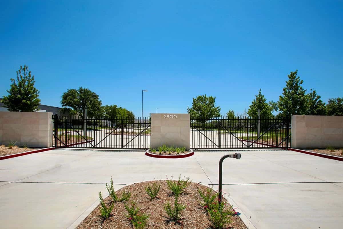 Secure gated entrance with trees and blue sky.