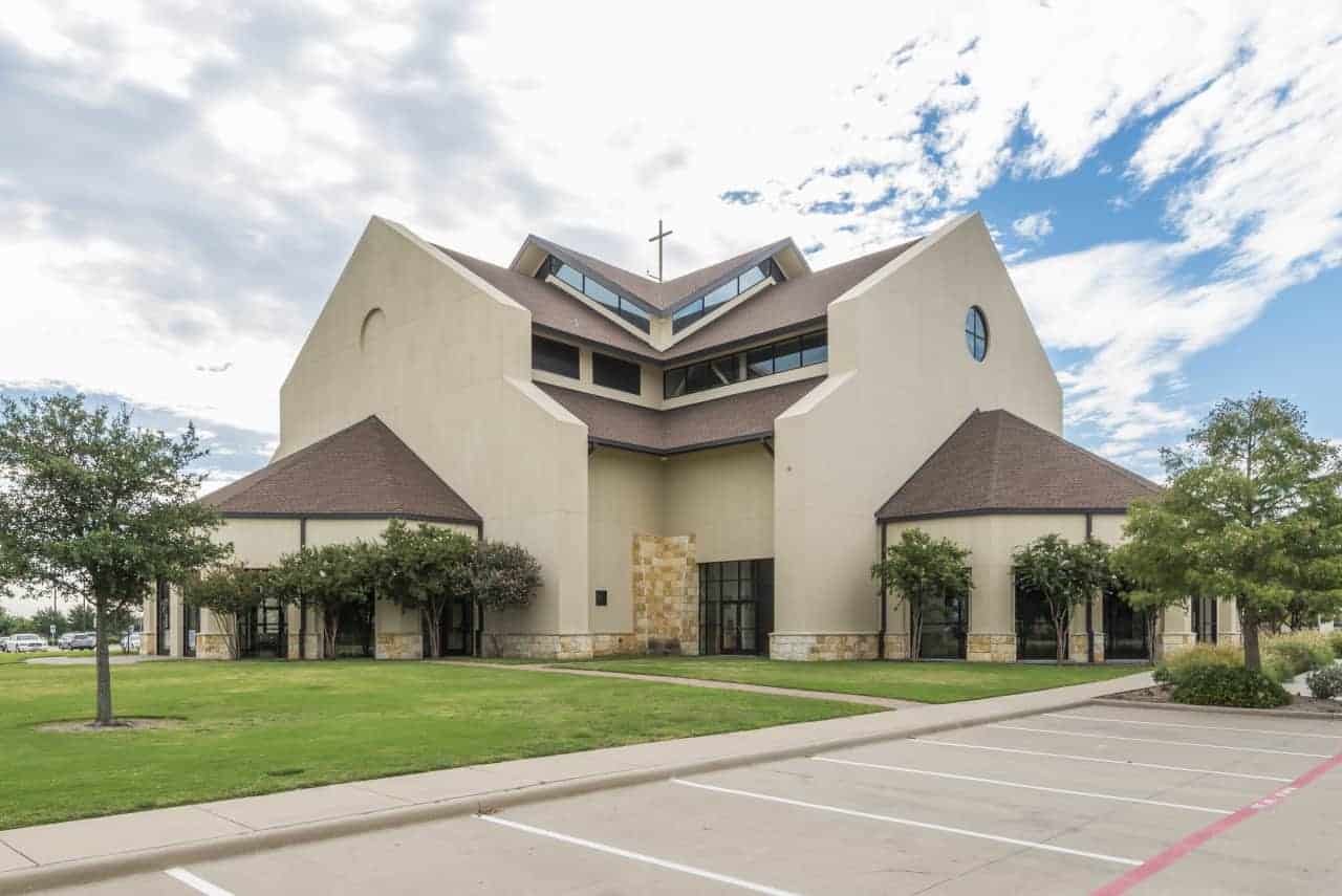 Modern church building with cross under cloudy sky.