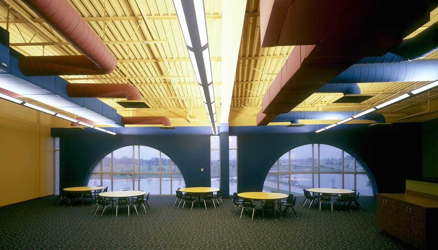 Modern cafeteria with colorful ceiling ductwork and tables.