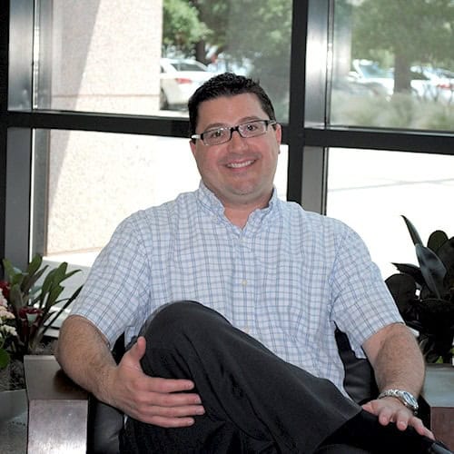 Smiling man sitting indoors by window.