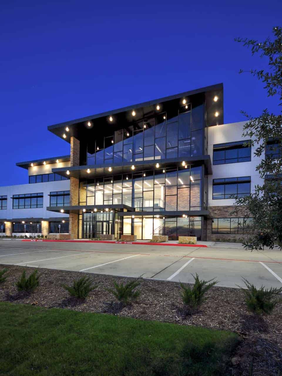Modern office building at dusk with lights on.