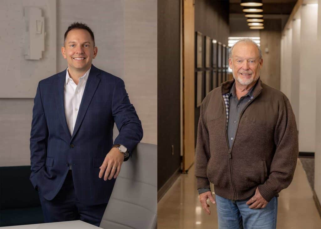 Two men standing, one in suit, one in sweater.