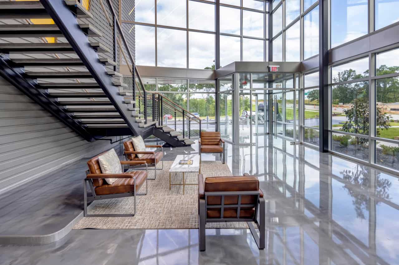 Modern glass office lobby with seating and stairs.
