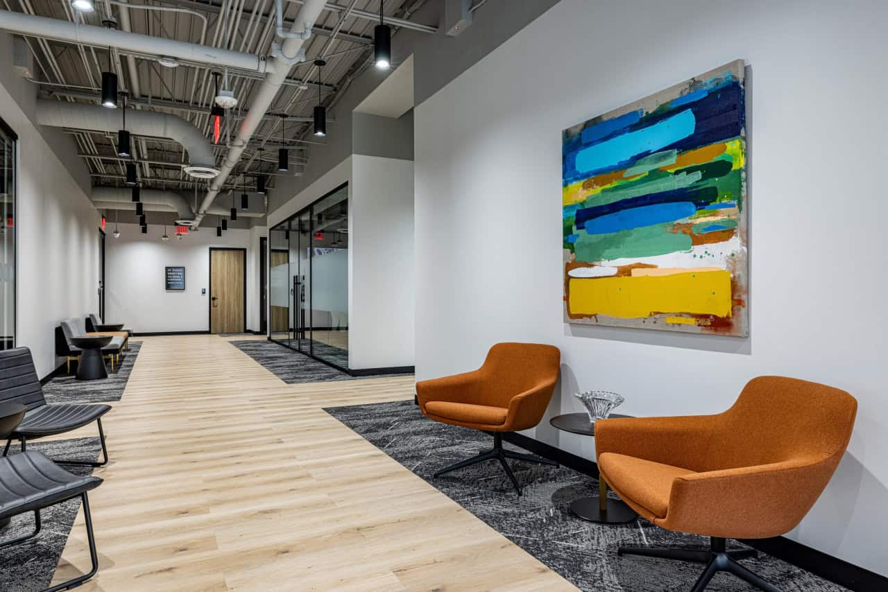 Modern office hallway with art and orange chairs.