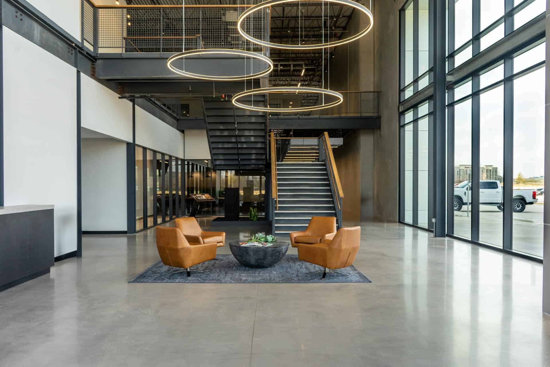 Modern industrial hotel lobby with sleek design, leather chairs, glass walls, and stylish lighting fixtures.