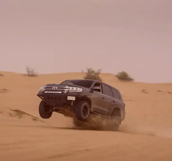 Toyota Land Cruiser driving over sand dunes in desert landscape.