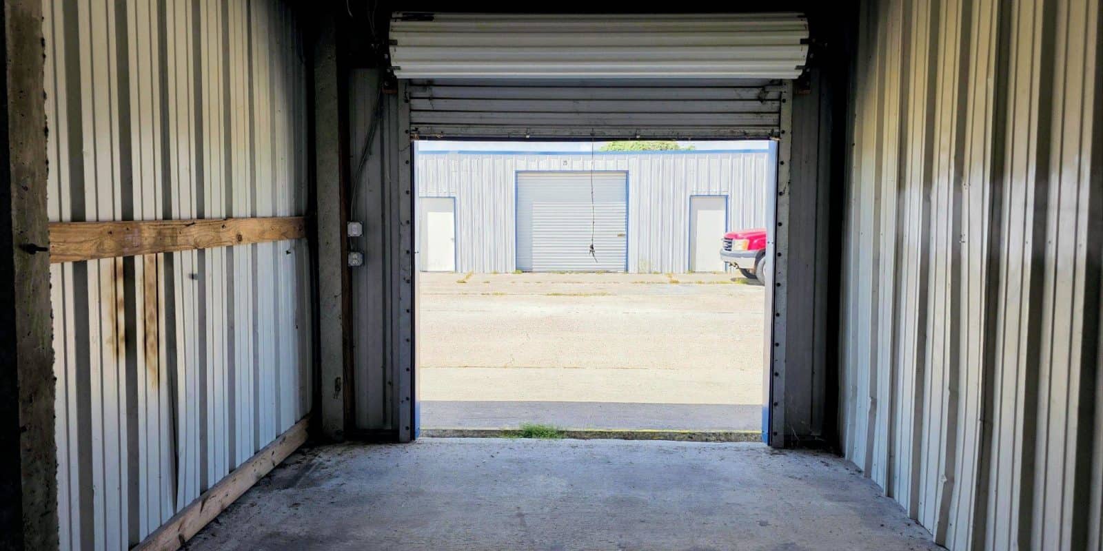 Aransas Pass RV Park and Storage Interior of Aransas Pass RV and Storage unit, roll-up door open to paved lot, multiple storage units, red car by drive-through spaces.