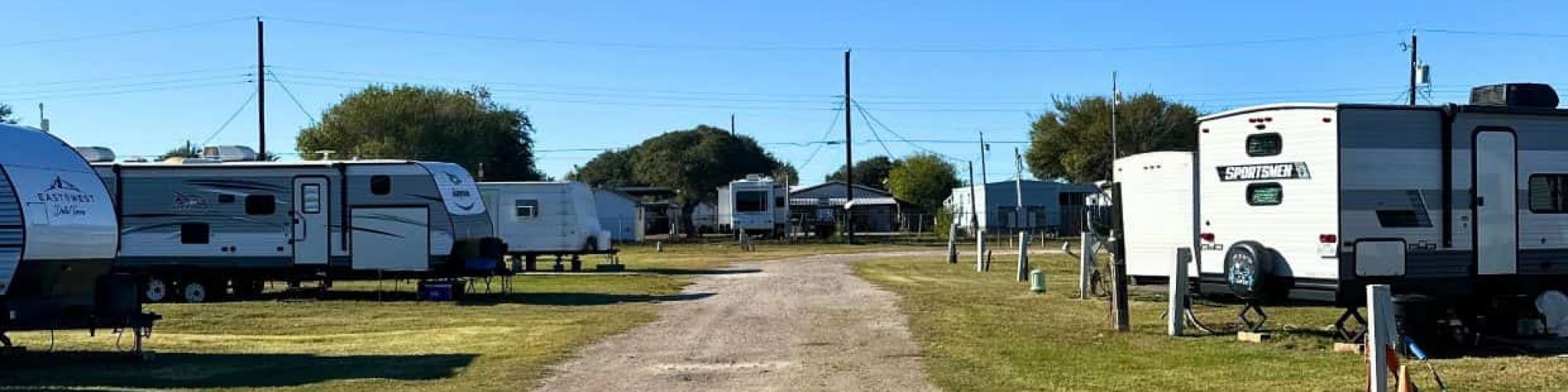 Aransas Pass RV Park and Storage Aransas Pass RV and Storage with gravel road, spacious RV sites on grass, storage units, trees, power poles under clear blue sky.