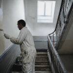 Ouvrier rénovant cage d'escalier immeuble avec peinture et garde-corps