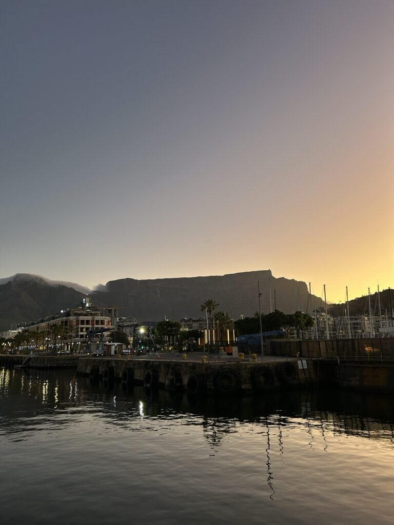 Table Mountain at sunset, taken from the Waterfront, with the harbour in the foreground, and orange and pink skies in the background.