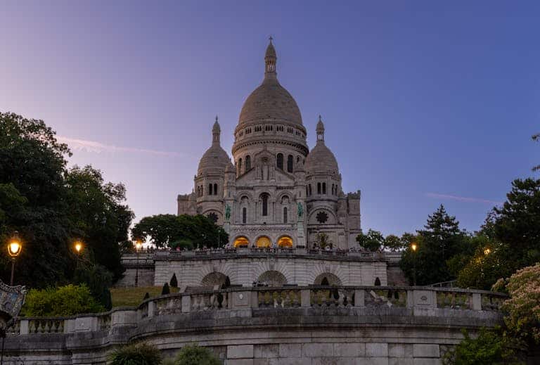 Beautiful view of Sacré-Cœur with evening lights, captured at twilight in Paris. Be aware of Paris scams at the Sacré-Cœur. Photo by Igor Passchier.