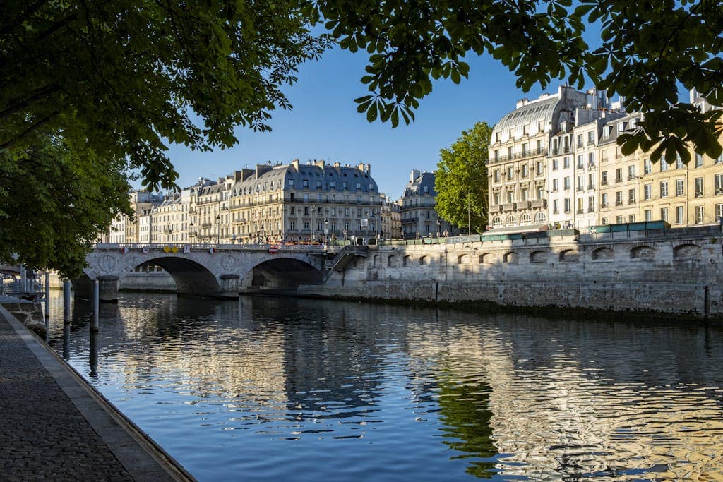 Charming Paris riverside view with historic architecture and reflections on the Seine under clear blue skies.  The Batobus, which travels along the Seine, is a scenic way to get around Paris.  Photo: Gheorghe Lupan