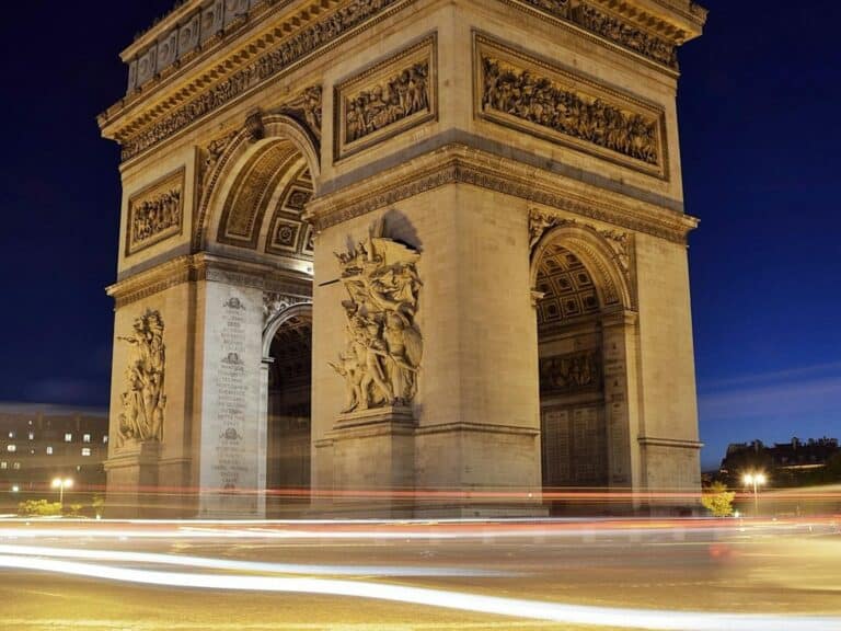 Elegant night shot of the Arc de Triomphe in Paris with light trails underneath, capturing its monumental beauty.