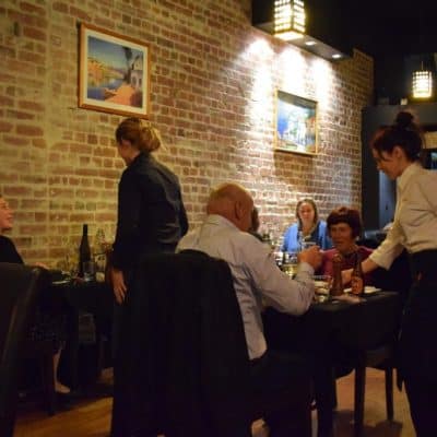 Cozy Italian restaurant interior with brick walls, diners enjoying meals, and servers providing attentive service.