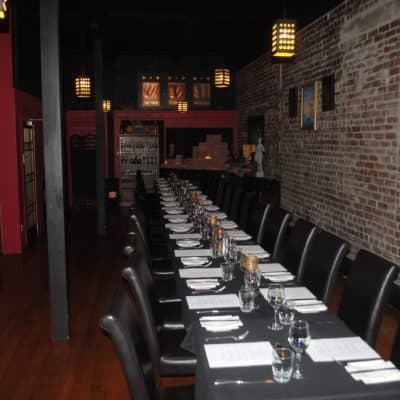 Elegant restaurant interior with a long table set for dining at Bella Vita, featuring black chairs and exposed brick walls.