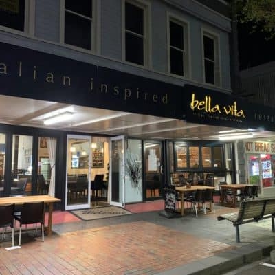 Bright evening view of Bella Vita Italian restaurant and bar with inviting outdoor seating on a sidewalk.