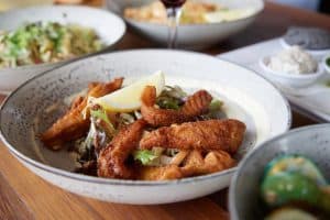 Crispy fried fish with fresh lemon, side salads, and dipping sauces at Bella Vita restaurant in New Zealand.
