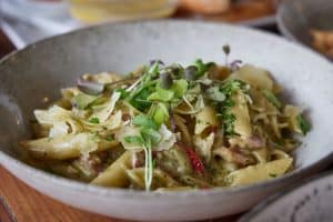 Creamy pasta with fresh microgreens and herbs, served in a rustic bowl, perfect for dining at Bella Vita.