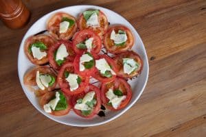 Fresh tomato and mozzarella salad with basil on a white plate, served with balsamic glaze, on a wooden table.