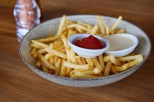 Golden French fries with ketchup and mayonnaise in a rustic ceramic bowl on wooden table.