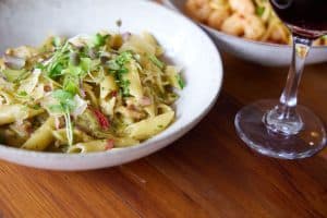 Delicious creamy pasta with fresh herbs and microgreens in a white bowl on wooden table.