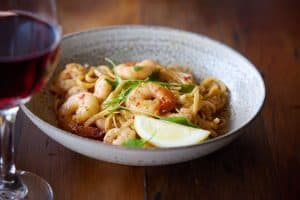 Tender seafood linguine with fresh herbs and lemon wedge, served with a glass of red wine. Perfect for a delightful dining experience.