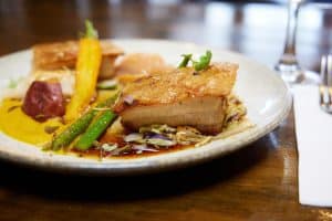 Succulent roast pork belly with vegetables and gourmet plating on a white dish.