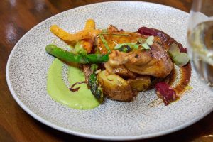 Savory chicken dish with roasted potatoes and colourful vegetables, served on a textured plate.
