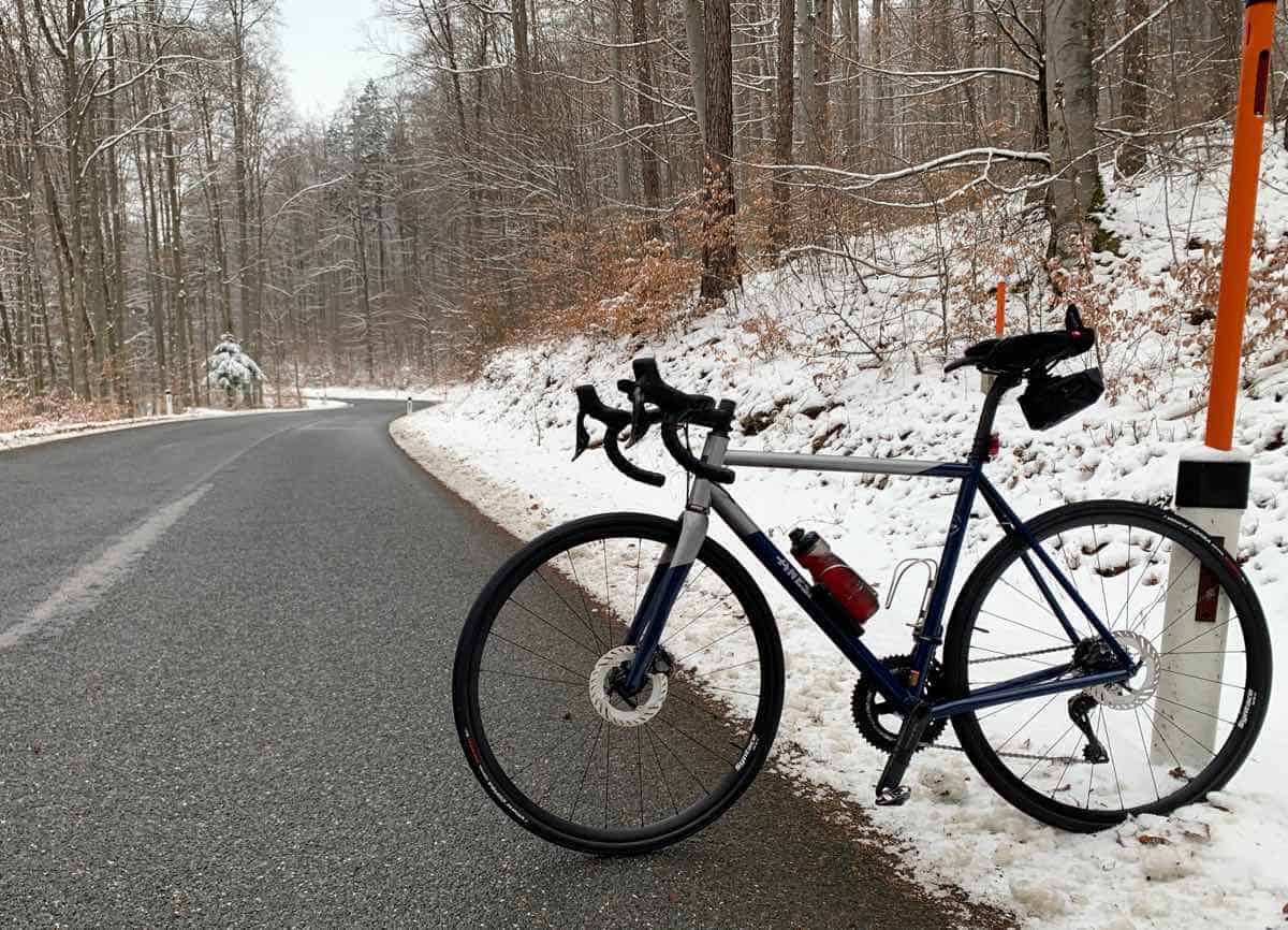Bicicletta da corsa su strada invernale in montagna con neve e alberi, outdoor cycling, attività sportive, Bici che Amore.