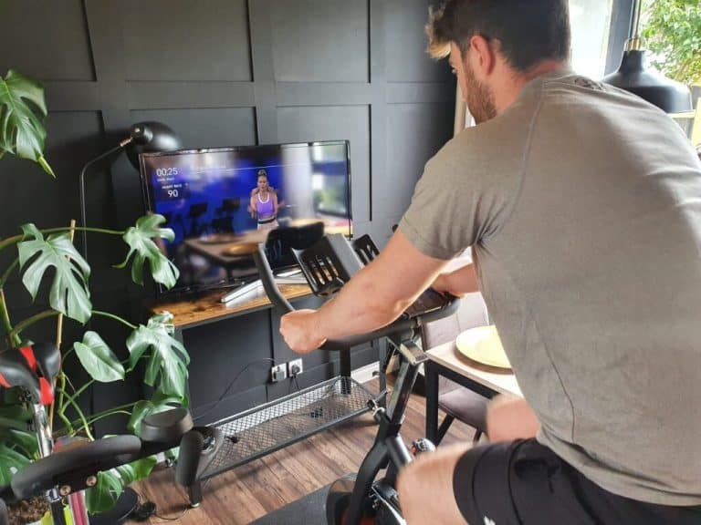 Allenamento indoor su cyclette per fitness e cardio, con uomo che si esercita a casa davanti alla TV. Attività sportiva, benessere, esercizio fisico, workout, salute.