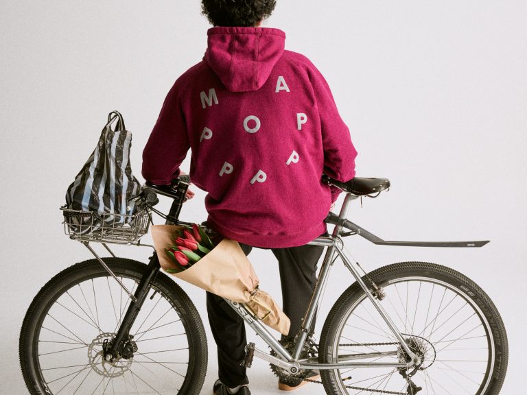 Ciclista con giacca rosa e bici da passeggio con borse e fiori, scena di biking urbano, stile casual e eco-friendly, immagini di bici e amore per il ciclismo, promozione di bici come modo di vivere sostenibile.