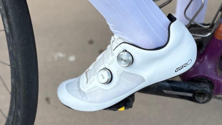 Scarpe da ciclismo bianche con attacchi SPD, focalizzate sul brand Giro, indossate da un ciclista, su una bicicletta da strada, simbolo di passione e amore per il ciclismo, perfette per chi cerca qualità e comfort.