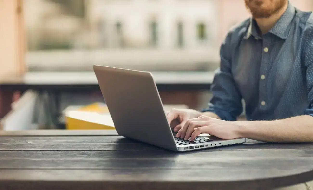 Man working on a laptop outdoors on a wooden table.