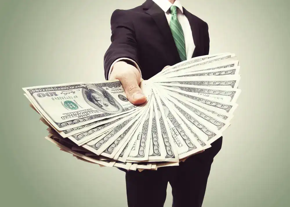 Businessman in suit holding a fan of $100 bills.