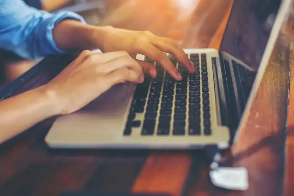 Person typing on a laptop keyboard, close-up of hands working on a computer.