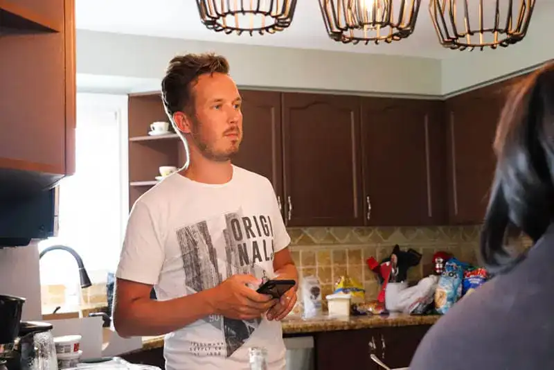 Young man holding smartphone in a modern kitchen setting.