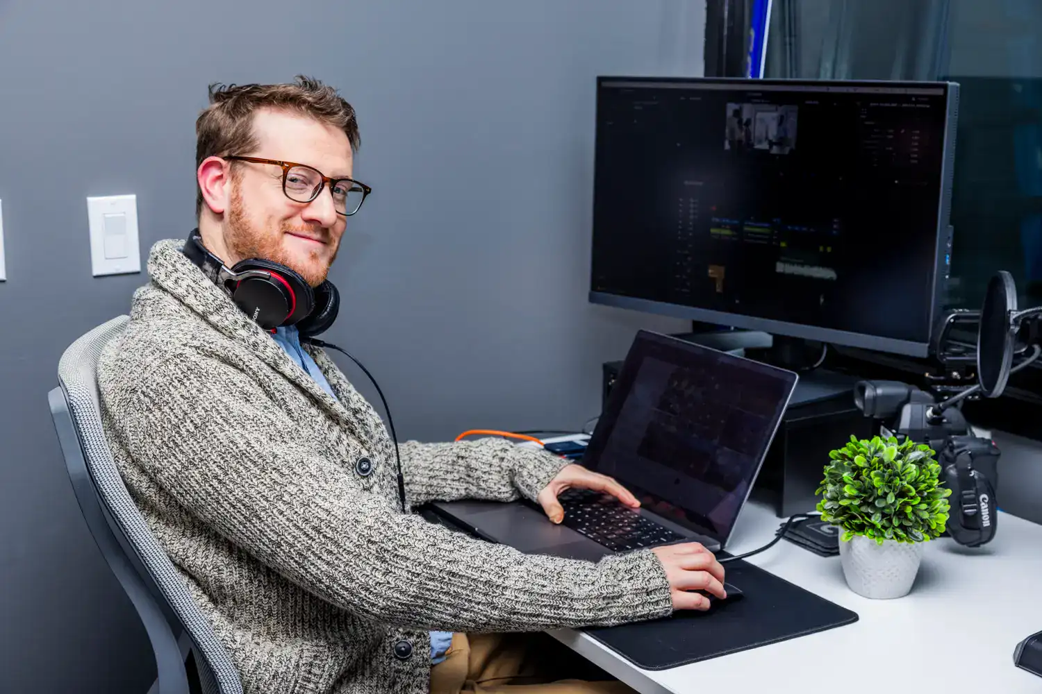 Man working on video editing software at a desk with dual monitors.