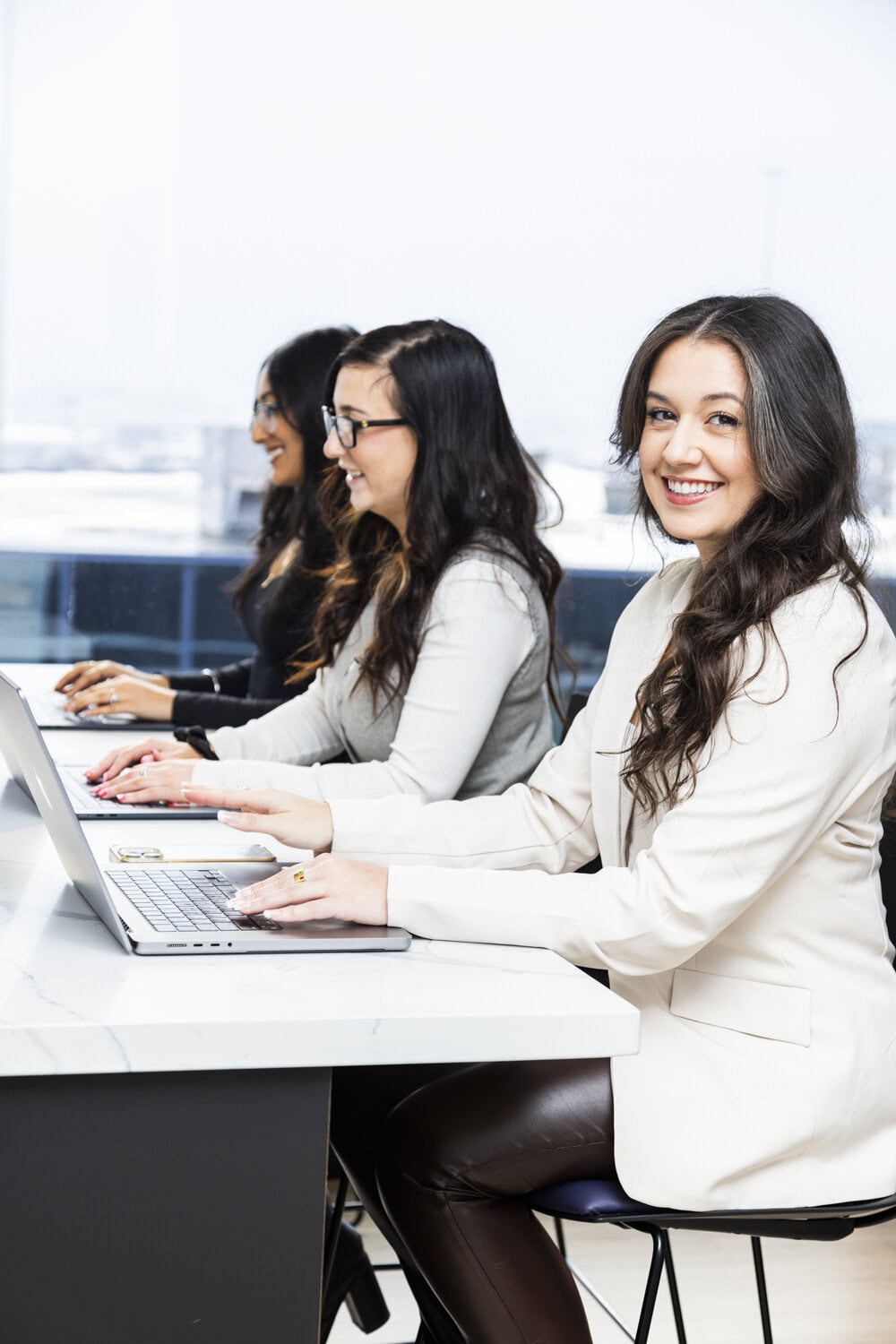 Group of young women working on laptops in a modern office setting.