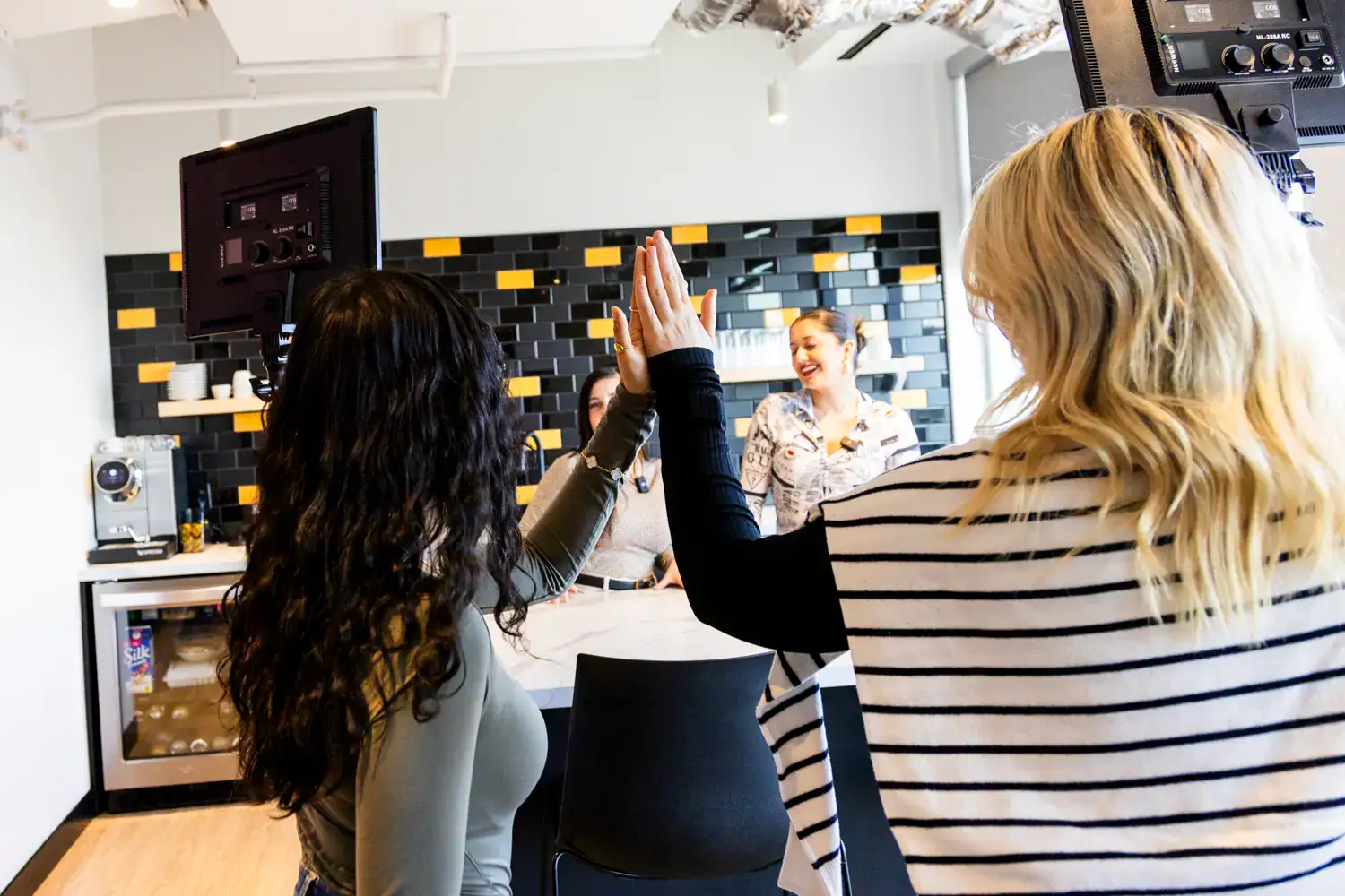 Two women high-fiving during a social media content shoot in a bright office.