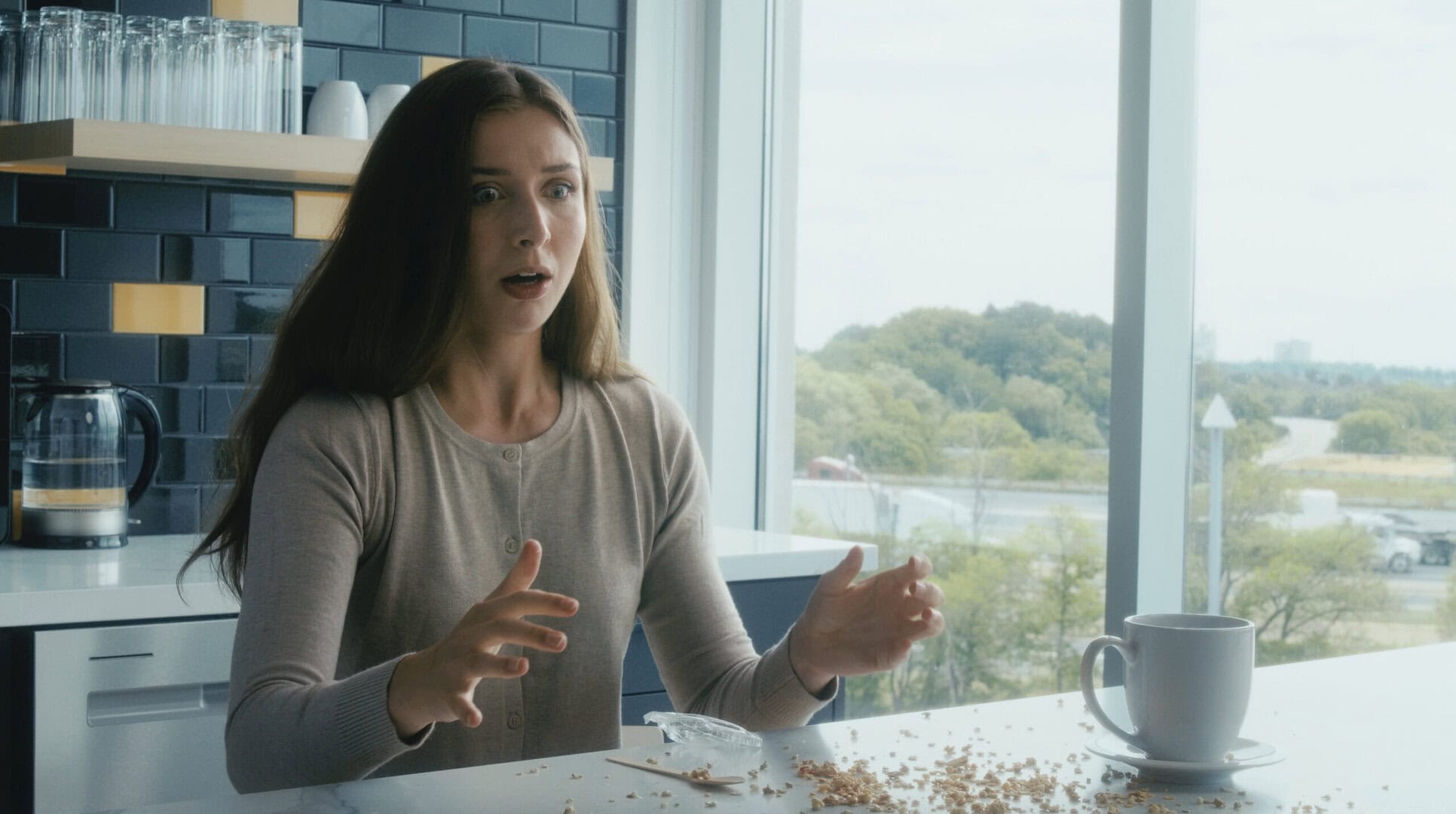 Woman spilling coffee in modern kitchen with large window view.