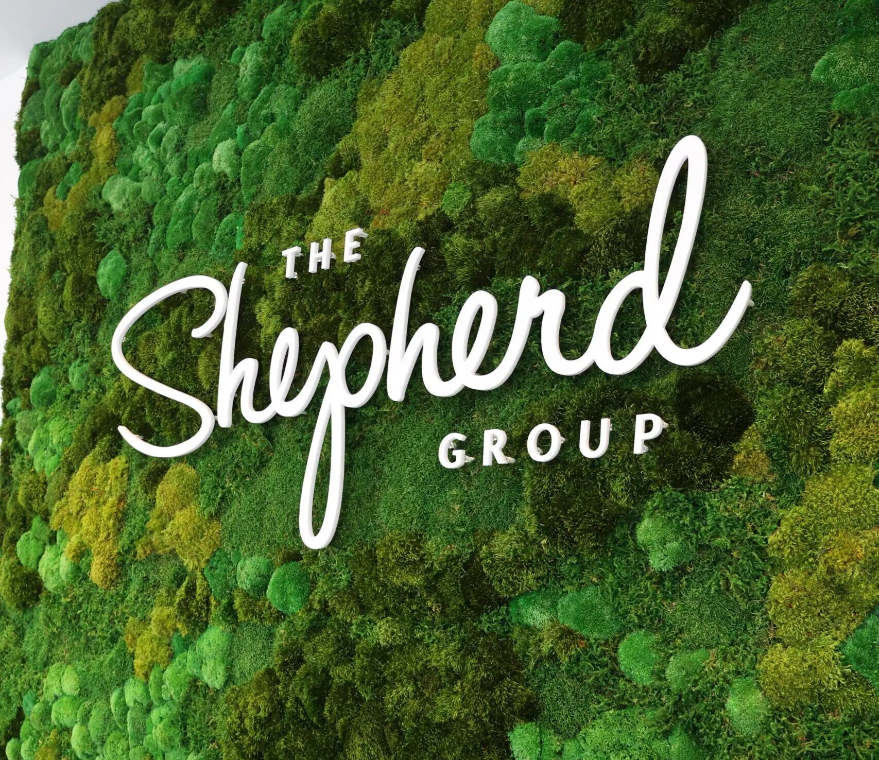 The Shepherd Group logo displayed on a lush green moss wall background.